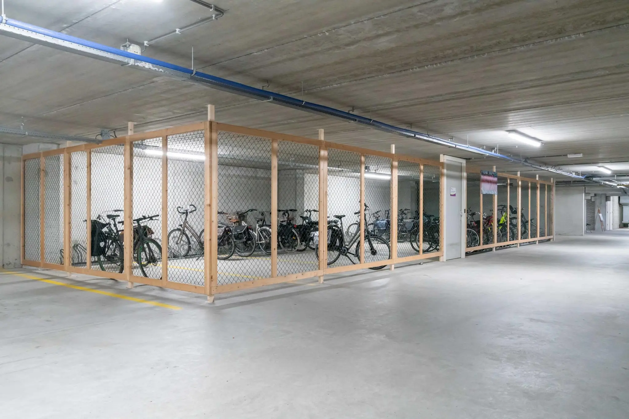 Afgesloten fietsenstalling met houten frame en gaas in een ondergrondse parkeergarage aan de De Bruyn Kopsstraat.
